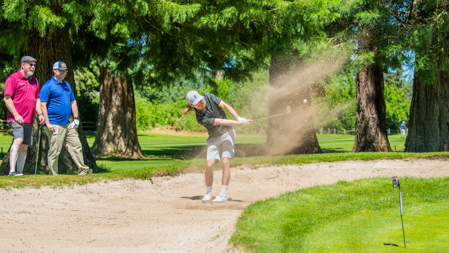 Michael Glasgo smiles as he makes contact with his ball through the sand Friday, during a charity tournament raising money for the Hope Alliance, at Riverside Golf Course in Chehalis.